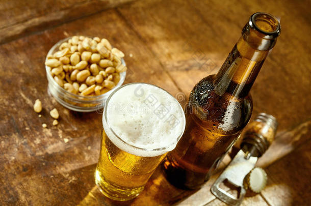 一杯啤酒放在桌子上，开瓶器和花生