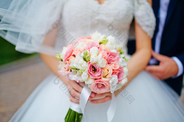 新娘牵着新郎的手和婚<strong>礼花</strong>束。 专注于婚<strong>礼花</strong>束。 按胸部和腿部裁剪。 穿婚纱的新娘