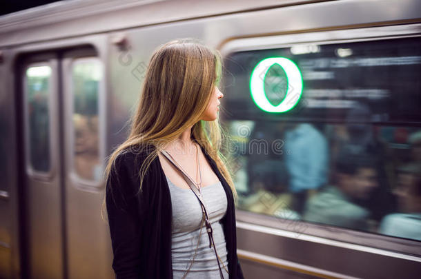美丽的女人站在地铁站看着到达的地铁列车