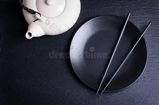 亚洲食物构图与中国筷子，茶壶和空盘在一个黑暗的石头背景