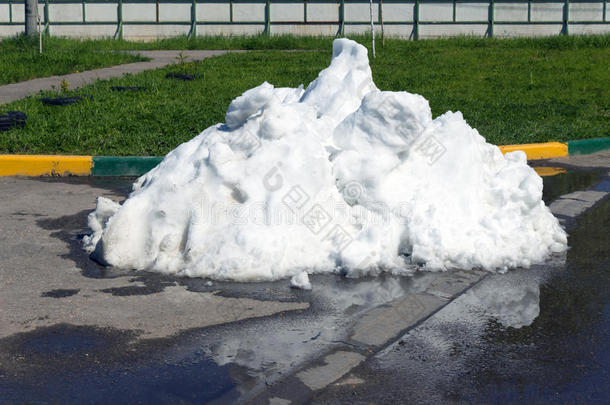 一堆脏雪躺在沥青路上的水坑里