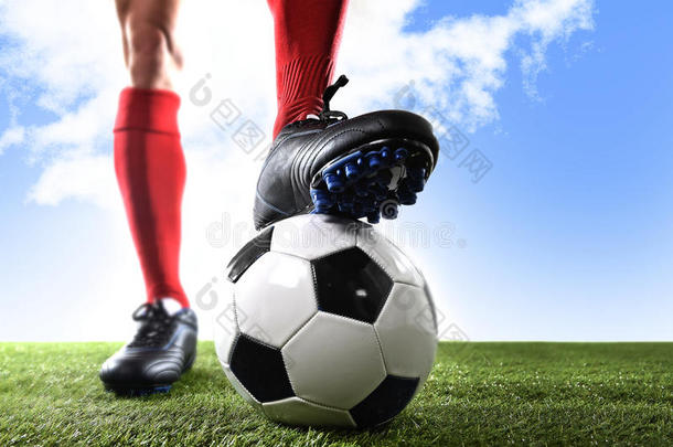 近景腿脚足球运动员穿着红色防弹服和黑色鞋子站在户外草地上与球合影