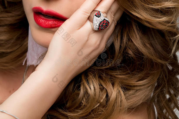 一个女人的嘴唇和带戒指的手的大肖像。 戒指上有宝石，银色和红色。 脸，红嘴唇