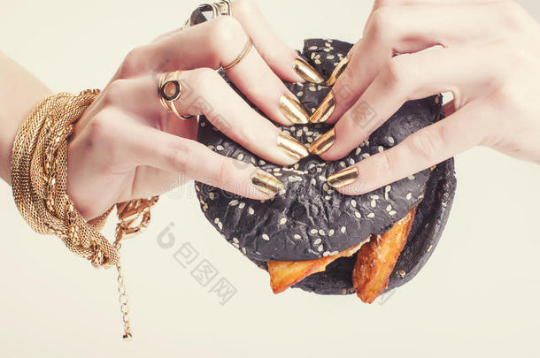 富有的女人手拿着金色的指甲和珠宝，手拿着黑色的汉堡包