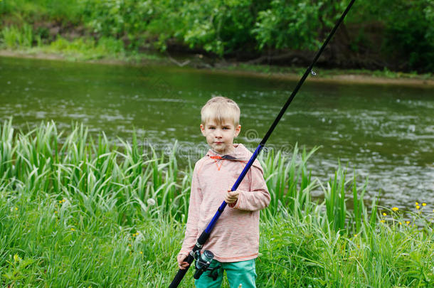 可爱的<strong>小</strong>男孩站在<strong>河边</strong>，手里拿着鱼竿。