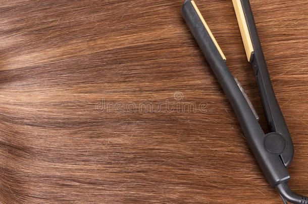 头发矫直机平放在棕色头发的背景上。