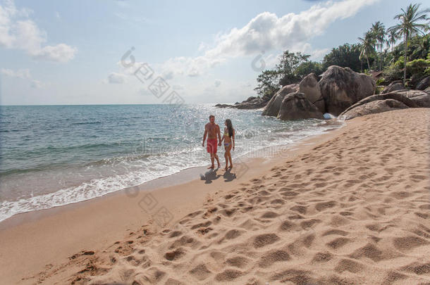 一对夫妇在海滩上散步。 年轻的幸福夫妇在海滩上散步，微笑着互<strong>相拥</strong>抱。