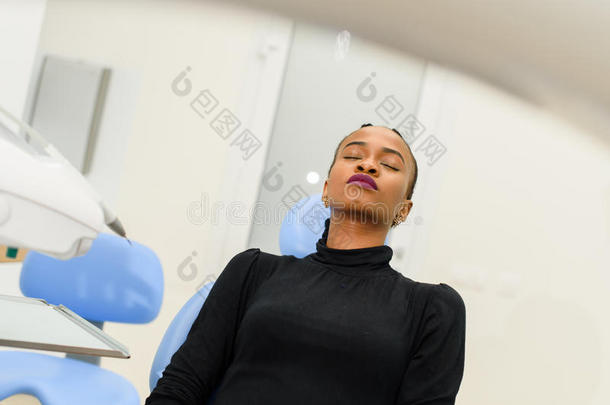 非洲裔美国黑人病人闭着眼睛坐在牙科椅上等牙医