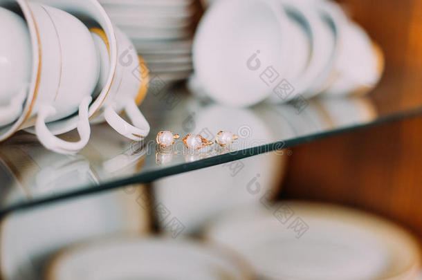 极端特写<strong>黄金珠宝</strong>点缀在玻璃橱柜架子上的珍珠。 波塞莱恩杯和盘子在背景
