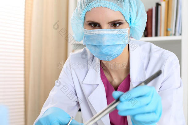美丽的女外科医生戴着口罩，拿着针，钳子和镊子