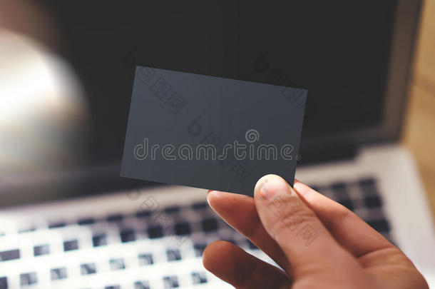特写照片男子显示空白黑色名片和使用现代笔记本电脑模糊背景。 准备好私人模型