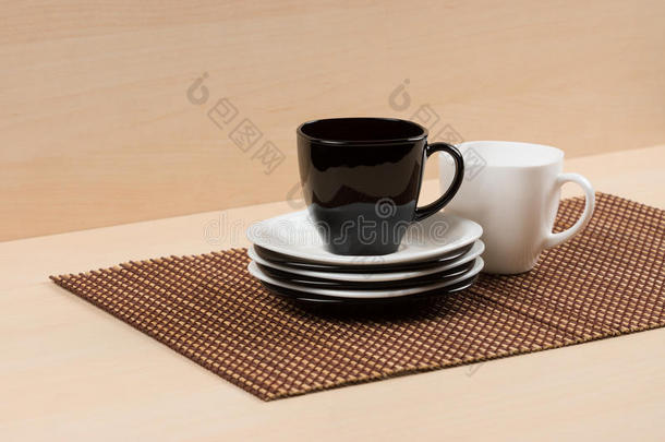 红茶杯在白色和黑色盘子的堆叠上，靠近白色茶杯的桌面上。