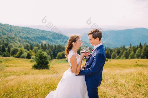 欢快的新婚夫妇在户外喝酒，庆祝他们的婚姻。 惊人的森林山丘作为背景