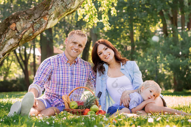 一对美丽微笑的夫妇带着儿子在草地上野餐