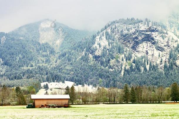 农舍的谷仓。春天的雪在草地上咆哮着群山。