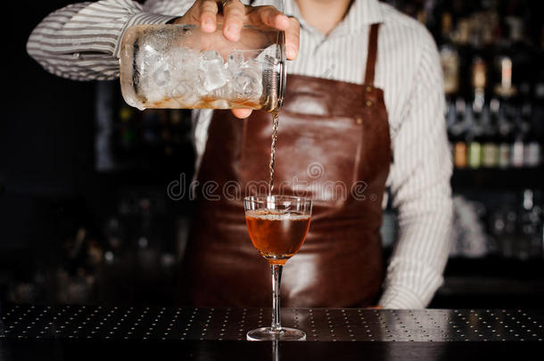 酒吧男招待把酒精鸡尾酒倒在玻璃杯里