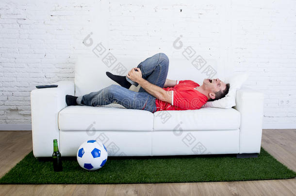 狂热的足球迷躺在沙发上，球铺在绿草地毯上，模仿足<strong>球场</strong>上的<strong>球场</strong>，痛苦地嘲笑球员
