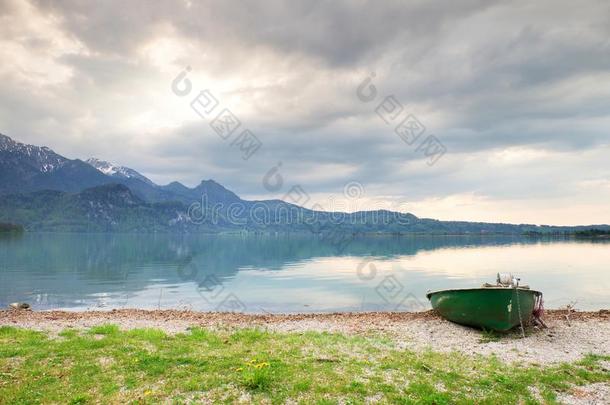 在阿尔卑斯山湖畔废弃的渔船。 早晨的湖面被阳光照耀着。