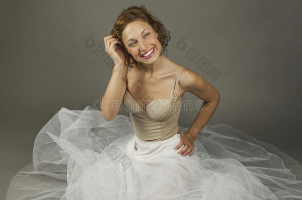 美丽的年轻富有表现力的芭蕾舞演员坐在地板上，穿着一件白色的<strong>长长</strong>的芭蕾舞裙
