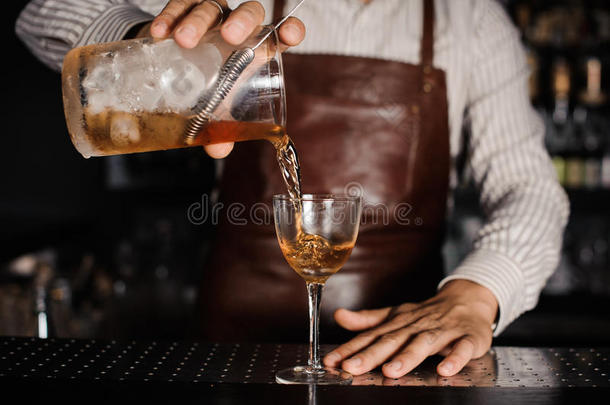 酒吧男招待把酒精鸡尾酒倒在玻璃杯里