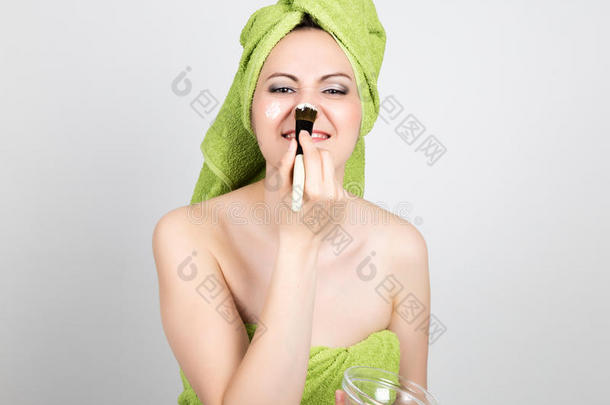 漂亮的年轻女人穿着<strong>浴巾</strong>在脸上做了一个化妆品面具。 美容行业和家庭护肤