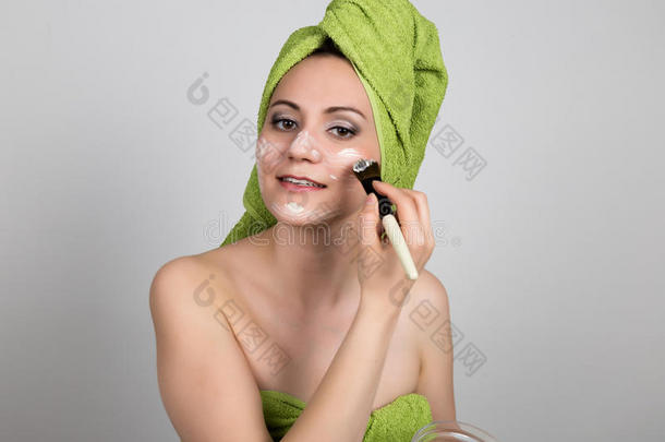 漂亮的年轻女人穿着浴巾在脸上做了一个化妆品面具。 美容行业和家庭护肤
