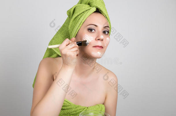 漂亮的年轻女人穿着浴巾在脸上做了一个化妆品面具。 美容行业和家庭护肤