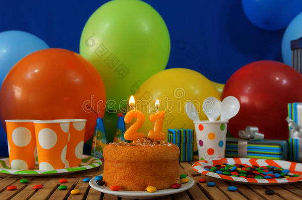 乡村木桌上的生日蛋糕，背景是五颜六色的气球、礼物、塑料杯和带糖果的塑料盘子