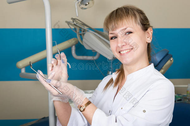 美丽的金发女子牙医拿着一件<strong>医疗器械</strong>。 <strong>背景</strong>中的牙科设备