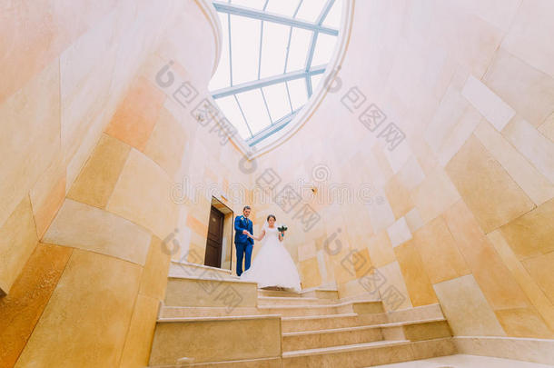 新婚夫妇在大理石楼梯上，背景是砂岩墙。 低角度