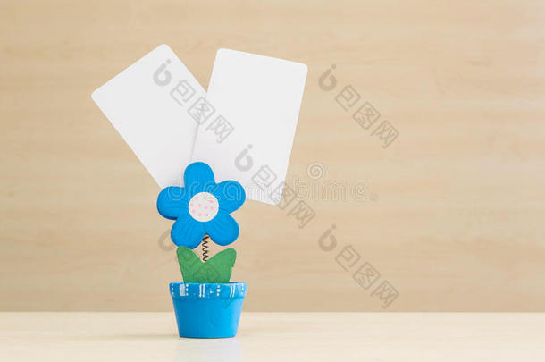 特写夹照片，蓝色花朵形状的花盆与黑色白纸在模糊的木桌和墙壁背景