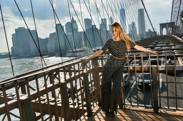 优雅的年轻女人穿着时髦的<strong>连体</strong>衣站在布鲁克林桥上。