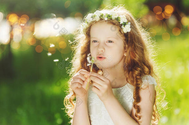 美丽的孩子穿着白色的连衣裙，在春天的公园里吹着蒲公英。