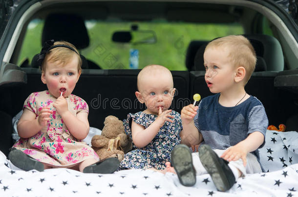 孩子们坐在汽车后备箱里。 三个孩子吃糖果。