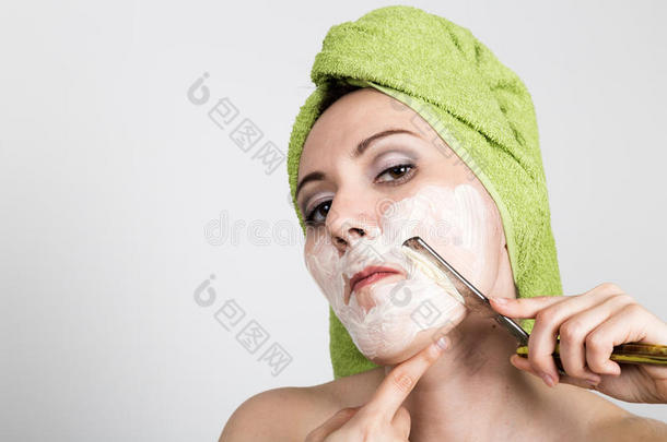 漂亮的年轻女人穿着浴巾，用直剃刀刮胡子。 美容行业和家居护肤理念