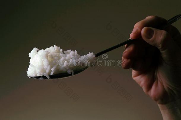 手拿着一个勺子，上面有煮熟的米饭