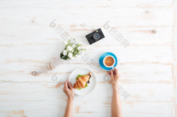 女人在木桌上用牛角面包喝咖啡的手