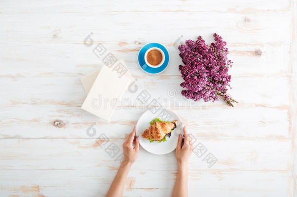 女人在桌子上吃牛角面包和喝咖啡的手