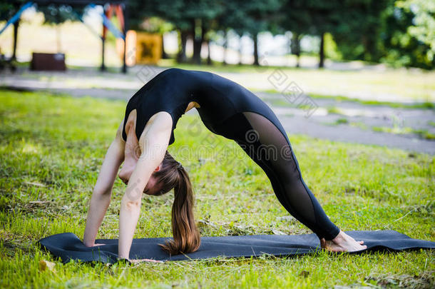 适合年轻漂亮的女人，穿着黑色运动紧身裤，在夏天的公园户外工作，做桥式