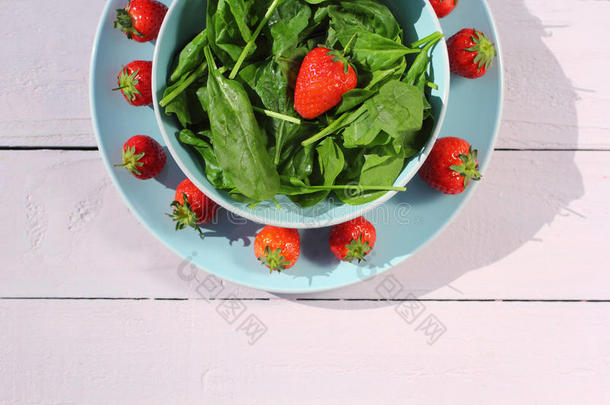 新鲜菠菜沙拉，菠菜和草莓放在木制浅粉色桌子上