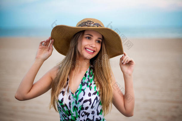 美丽的年轻微笑的女孩戴着帽子在海滩上。 快乐的女孩享受夏天的时间在沙滩上靠近海洋和举行