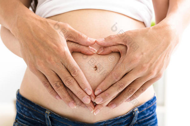 双手在怀孕的腹部形成双心的形状