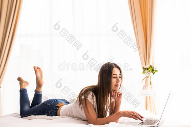 女孩躺在房间里的床上看着笔记本电脑显示器