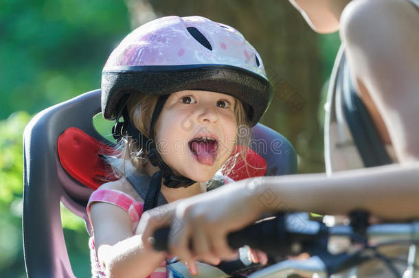 女孩乘坐儿童座椅，戴着粉红色自行车头盔，伸出舌头