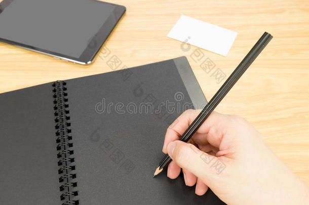 用手拿铅笔写在空白的黑色书上，上面有桌子和名片