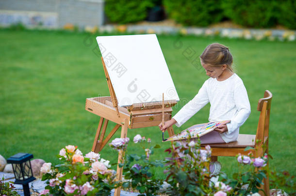 可爱的小女孩在户外画架上画一幅画。 热衷于她爱好的小艺术家。