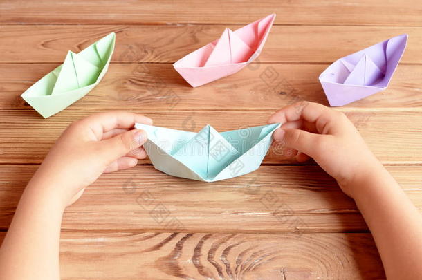 孩子手里拿着折纸船。五颜六色的船折纸放在木桌上