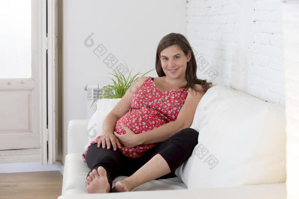 美丽快乐的8或9个月的孕妇躺在客厅沙发上，抱着大肚子
