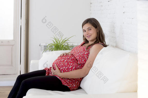 美丽快乐<strong>的</strong>8或9个月<strong>的孕妇</strong>躺在客厅沙发上，抱着<strong>大肚子</strong>
