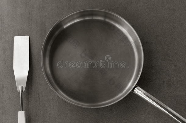 空<strong>不锈钢煎锅</strong>和刮刀俯视灰色背景，黑白照片